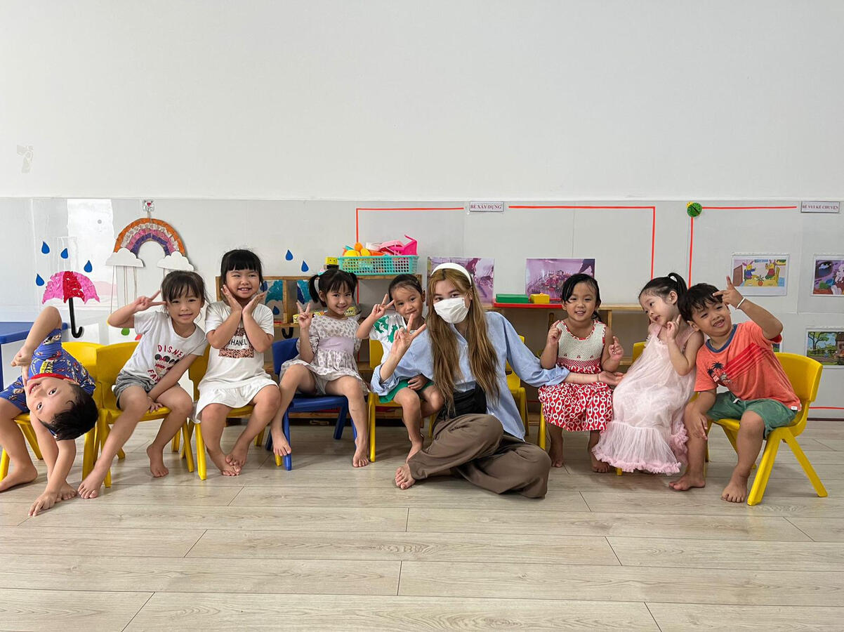 Lenny Cheng seated with a group of children while volunteering at a community centre in Vietnam, barefoot and smiling.
